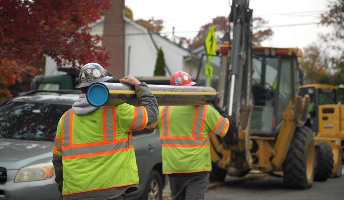 Two workers carry a new segment of gas line