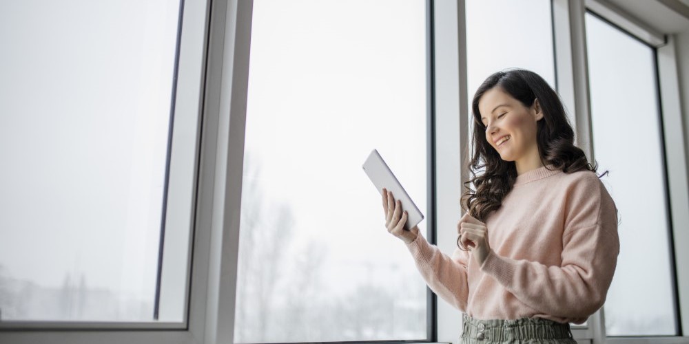 A woman looking at a tablet in front of a frosted window.